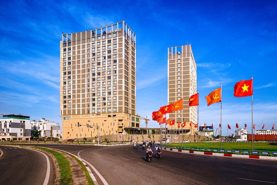 Hotel Nikko Hai Phong with twin towers, vibrant red flags, and a clear blue sky in the background.