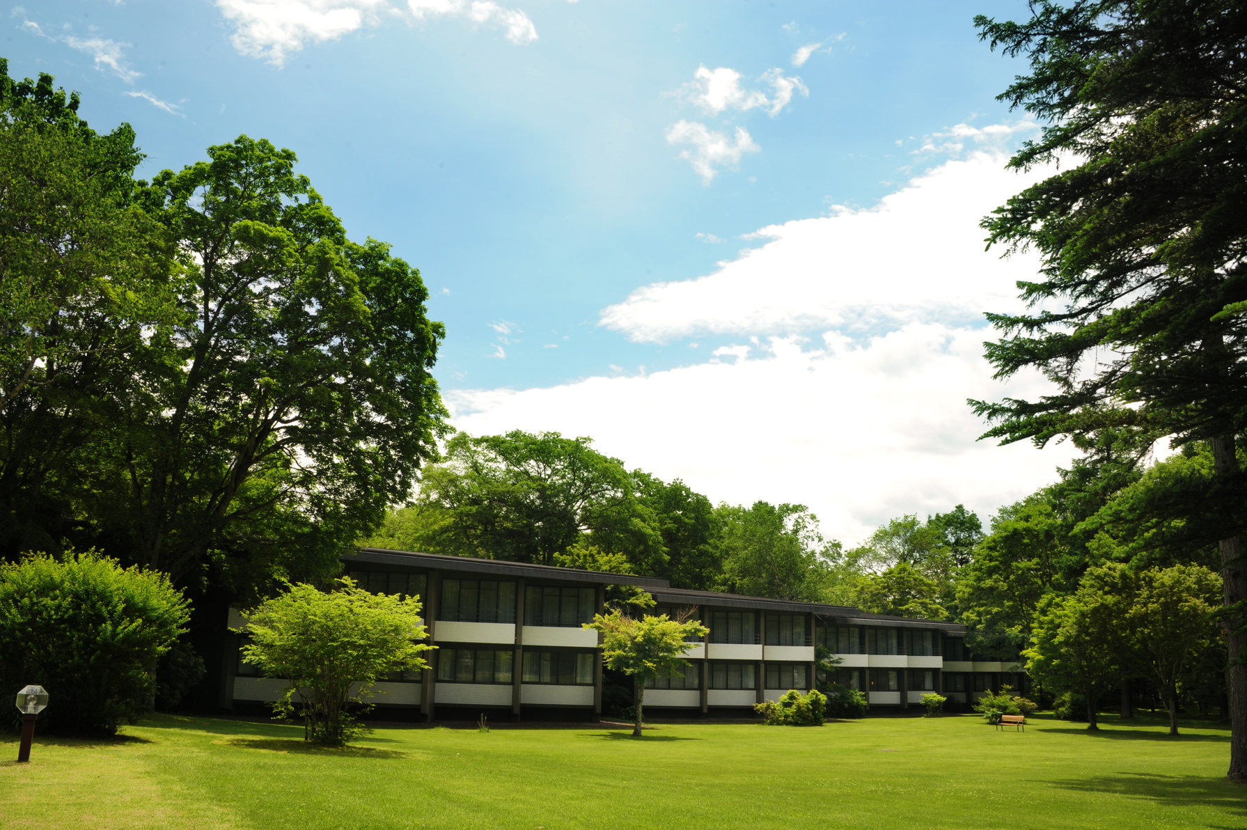 Hotel Kajima no Mori surrounded by lush trees and an open grassy lawn under a bright sky.
