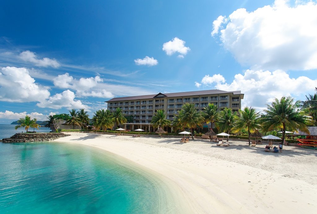 Beachfront view of Palau Royal Resort with palm trees and lounge chairs.