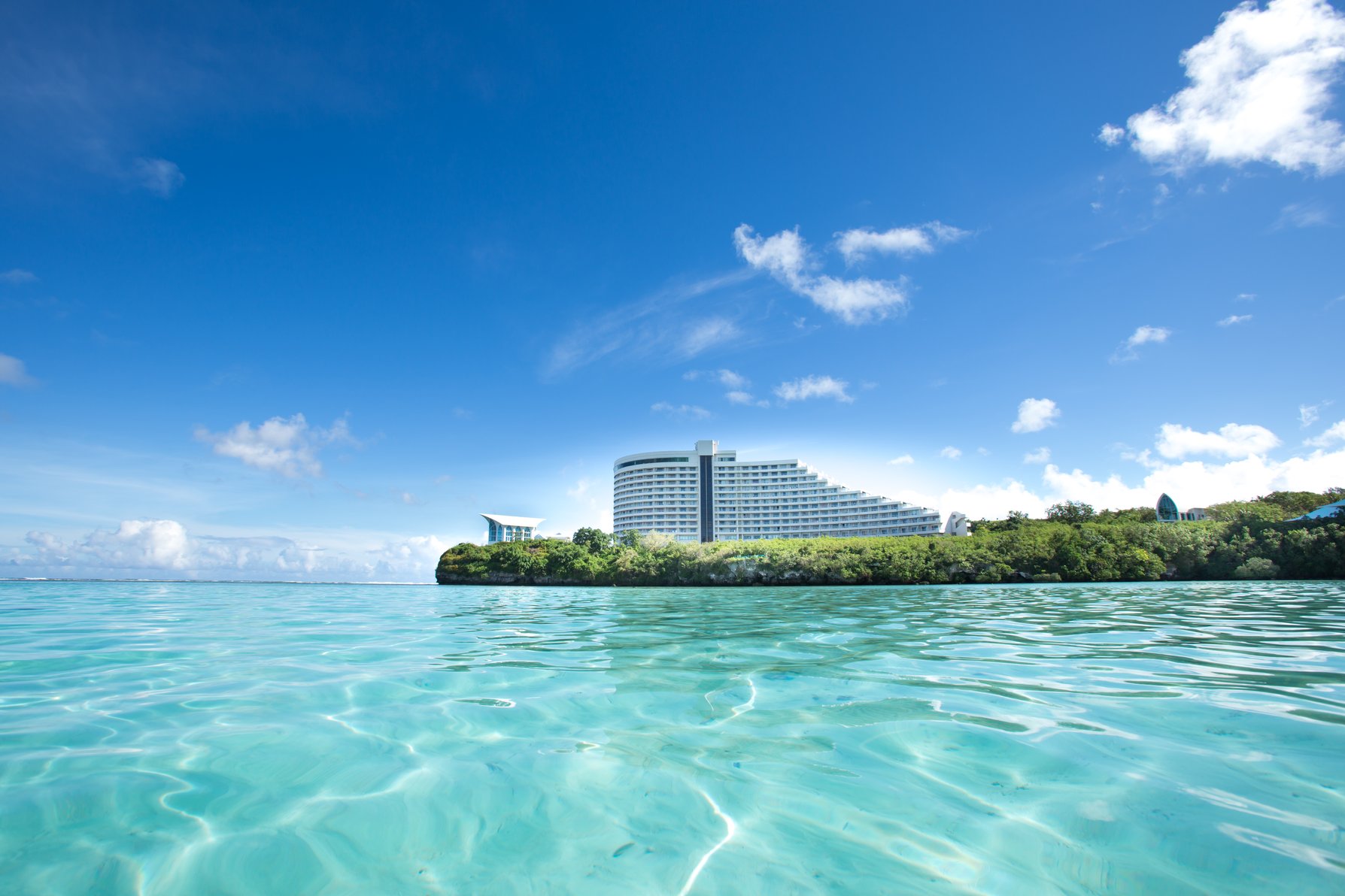 Hotel Nikko Guam viewed from clear turquoise ocean waters under a blue sky.