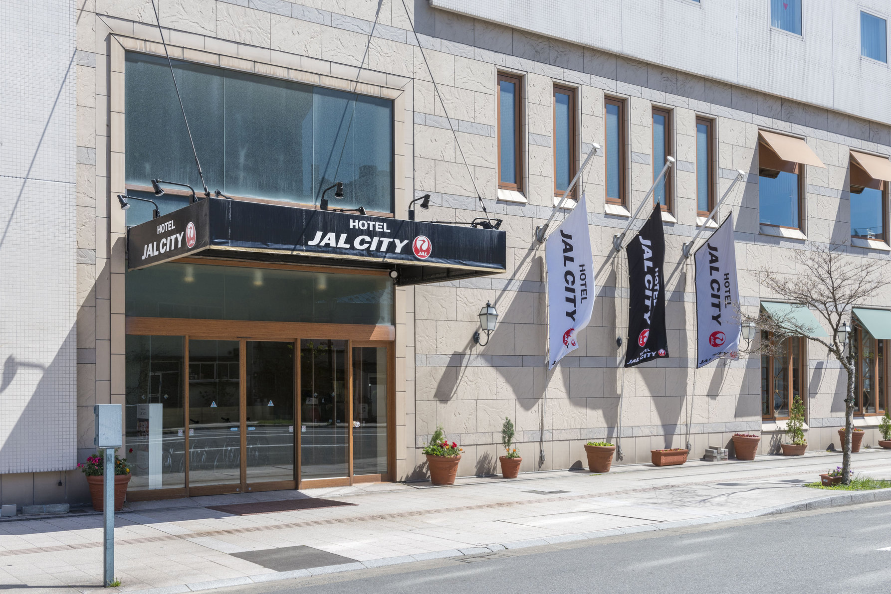 Entrance of Hotel JAL City Aomori with glass doors, signage, and flags displaying the hotel name.