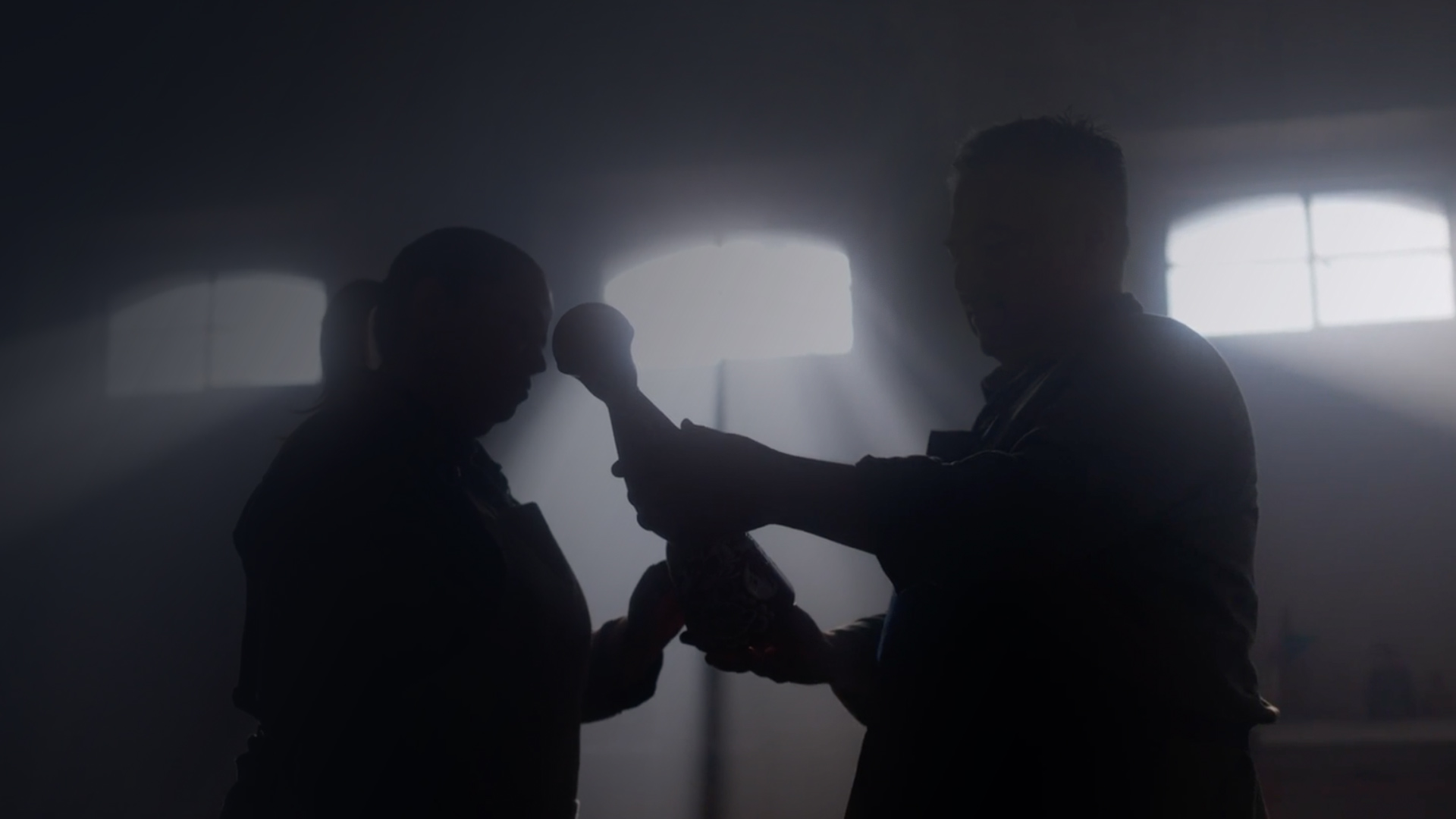 A black-and-white image of the silhouettes of two people holding a tequila decanter.