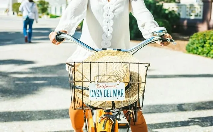 woman on a bike with a sun hat in the front basket with a CA plate on the front