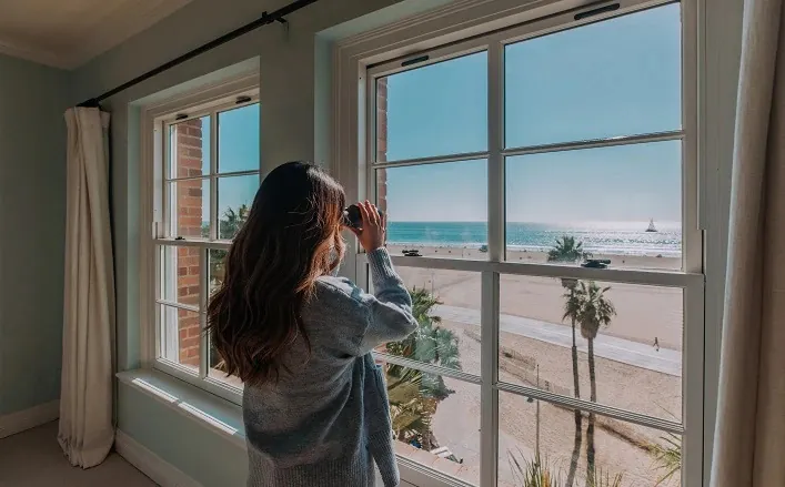 woman with binoculars looking out the penthouse window at the ocean