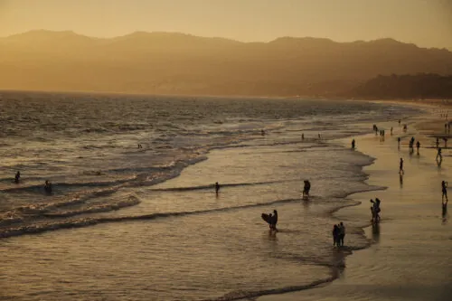 sunset view of the ocean waves and mountains, with people walking the beach