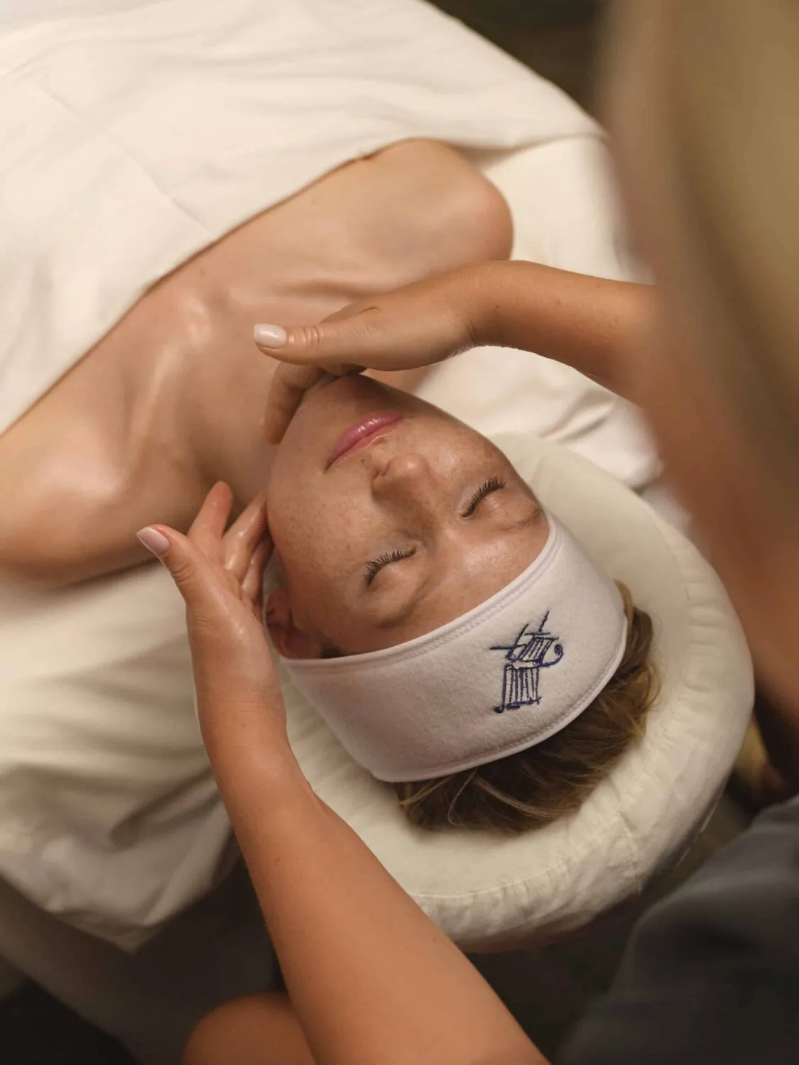 Woman wearing a spa headband receiving a facial massage.