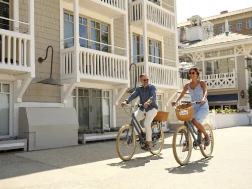 A couple riding bicycles in front of Shutters on the Beach hotel on a sunny day.