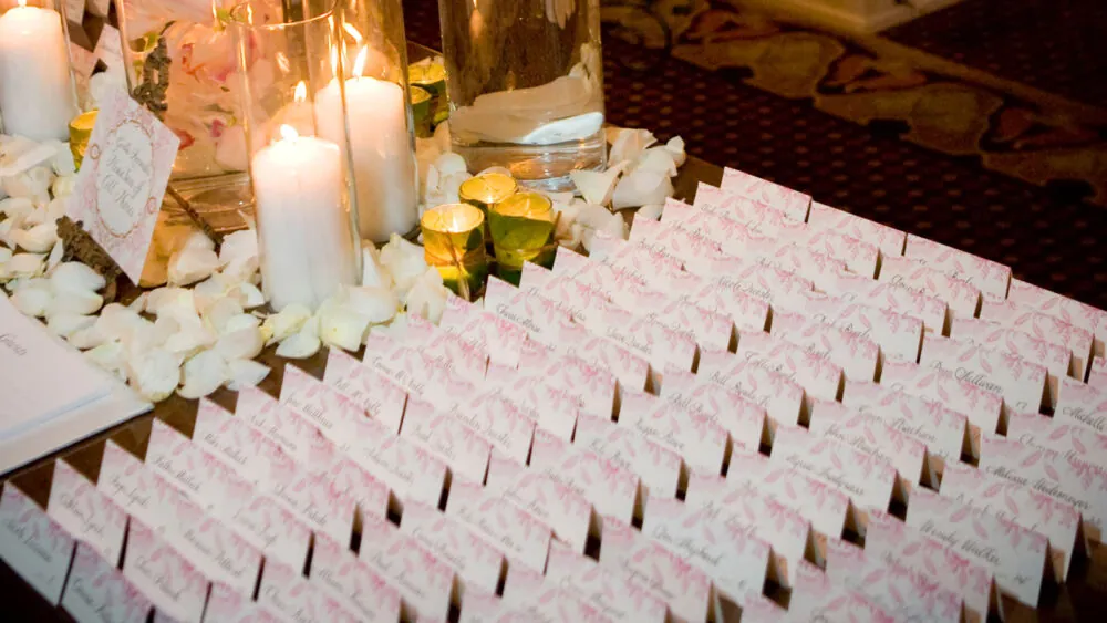 White and pink guest cards on a table decorated with candle lights and rose petals.
