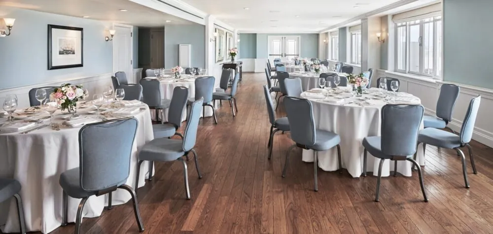 A white and blue dining room with round tables, elegantly set for an event.