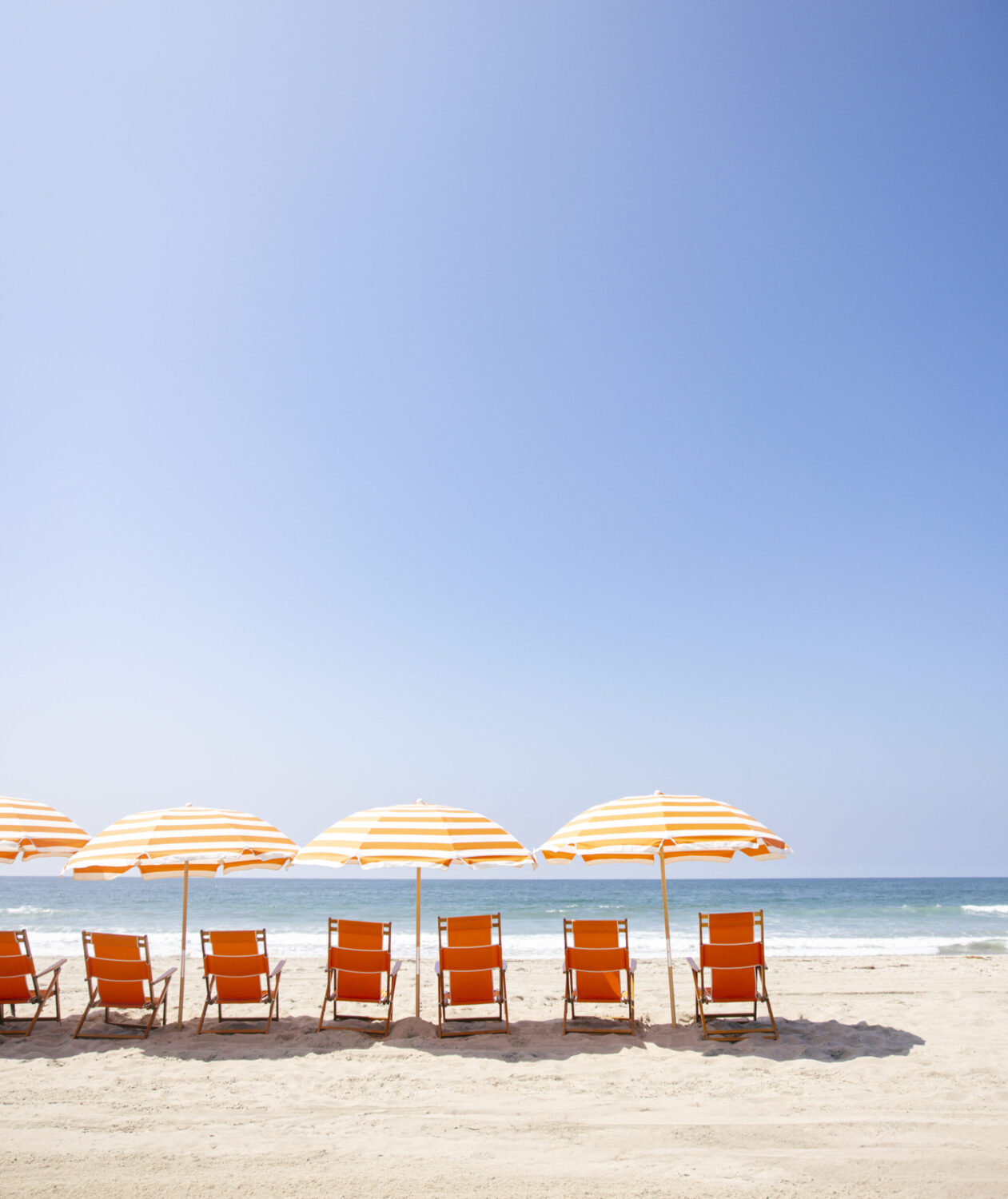 Row of orange beach chairs and striped umbrellas lined up by the ocean.
