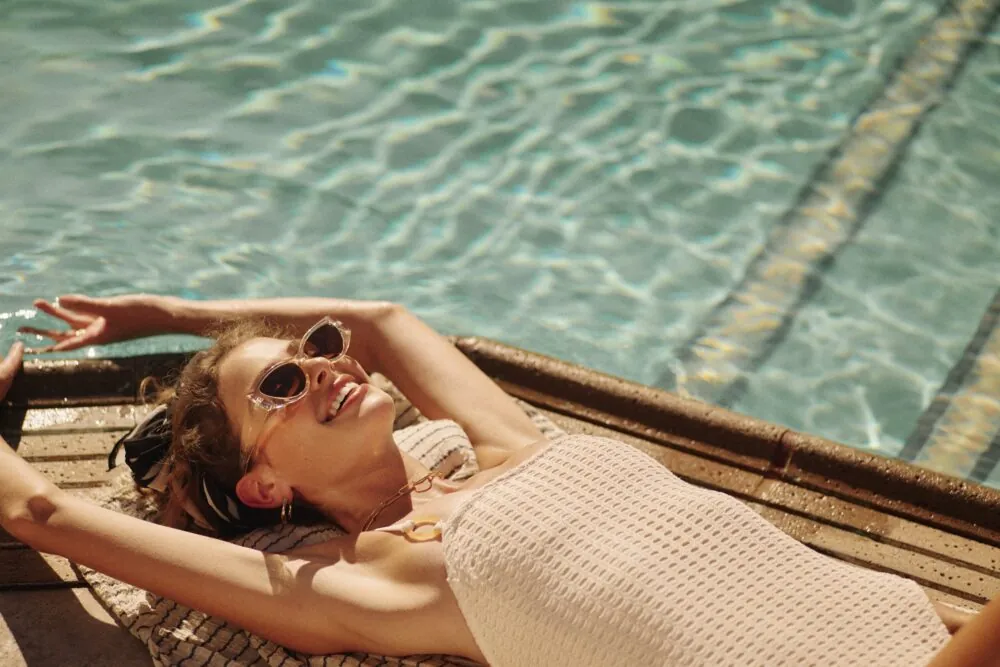 woman laying by the pool in a swimsuit with her hands above her head