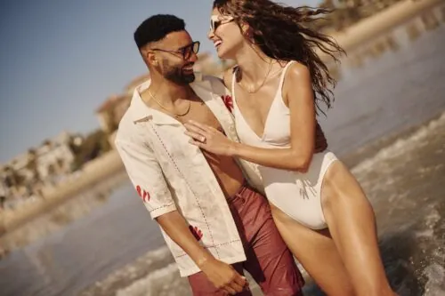 man and a woman laughing and facing each other, walking in the ocean