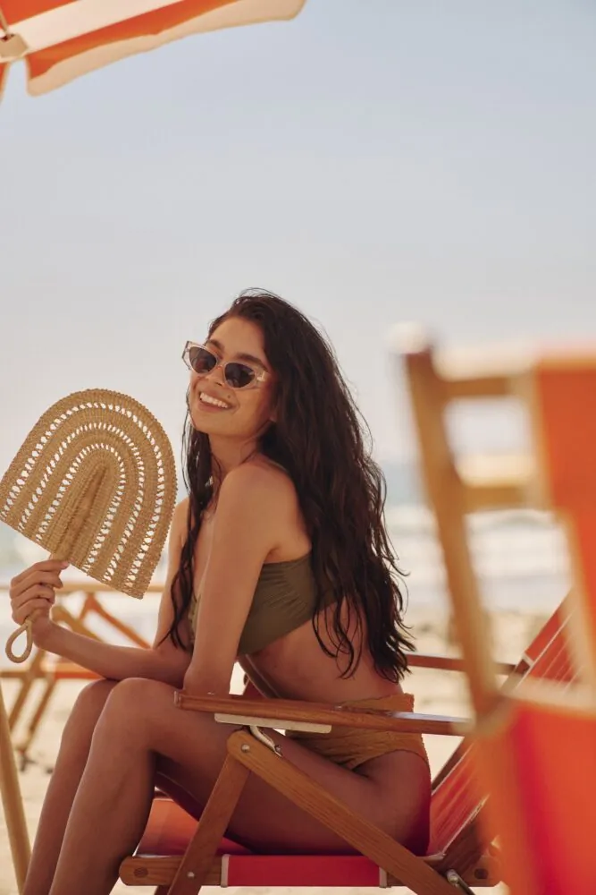 woman on the beach, sitting in a beach chair fanning herself with a crochet fan