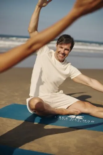 man doing a yoga pose, on the beach on a Casa del Mar yoga mat