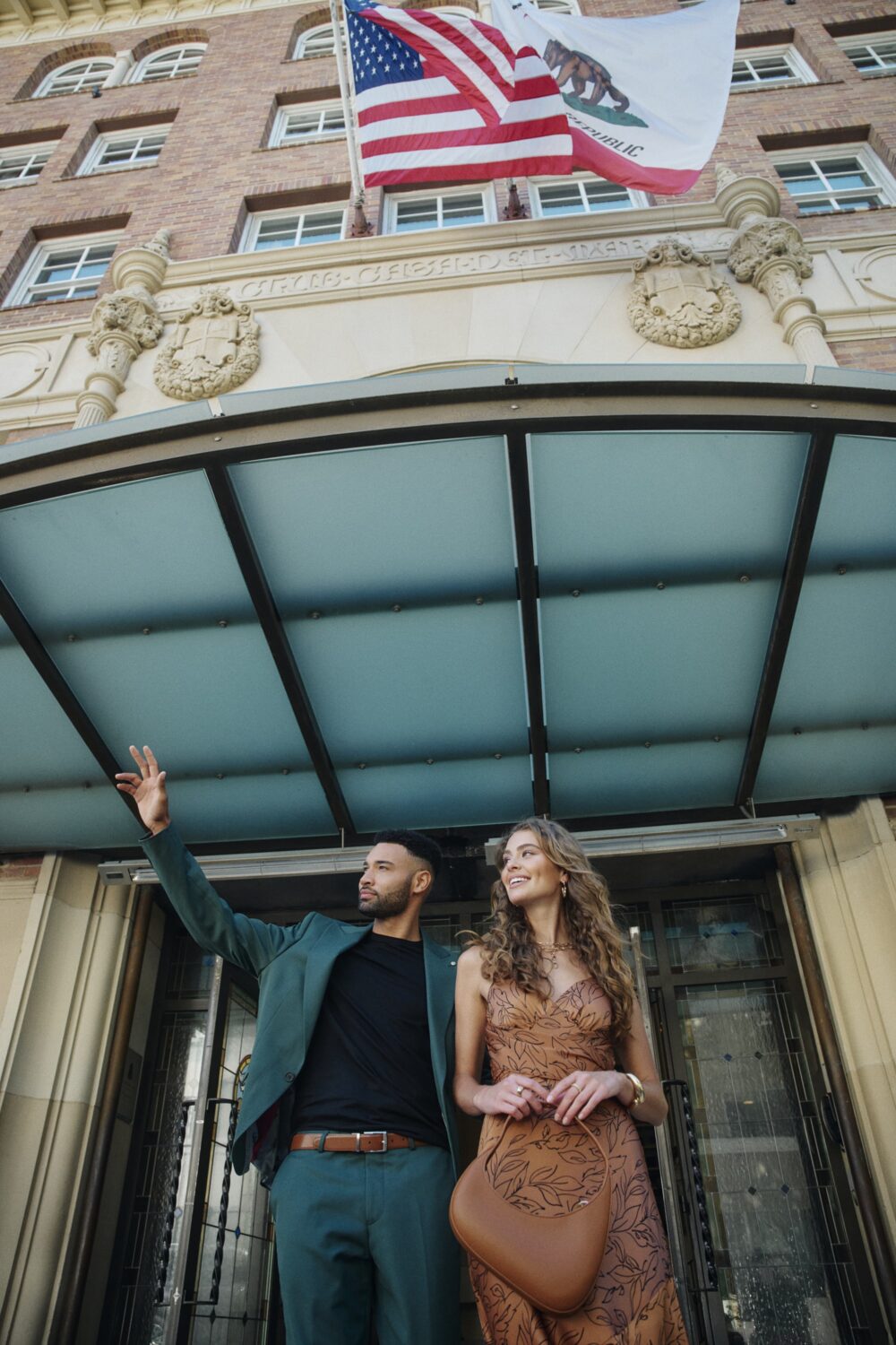 close up shot, from below, of a man and a woman walking out of the hotel's front entrance under the flags