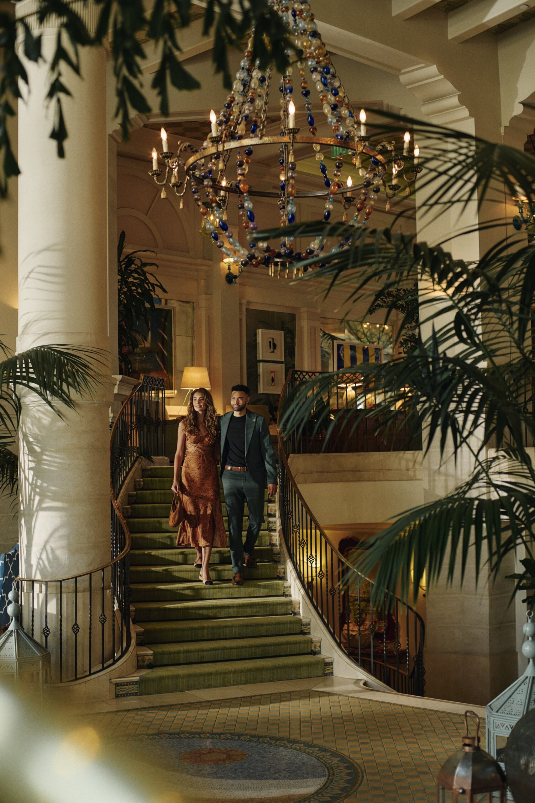 A man and a woman walking down the lobby stairs, dressed for dinner, with a mosaic tiled floor