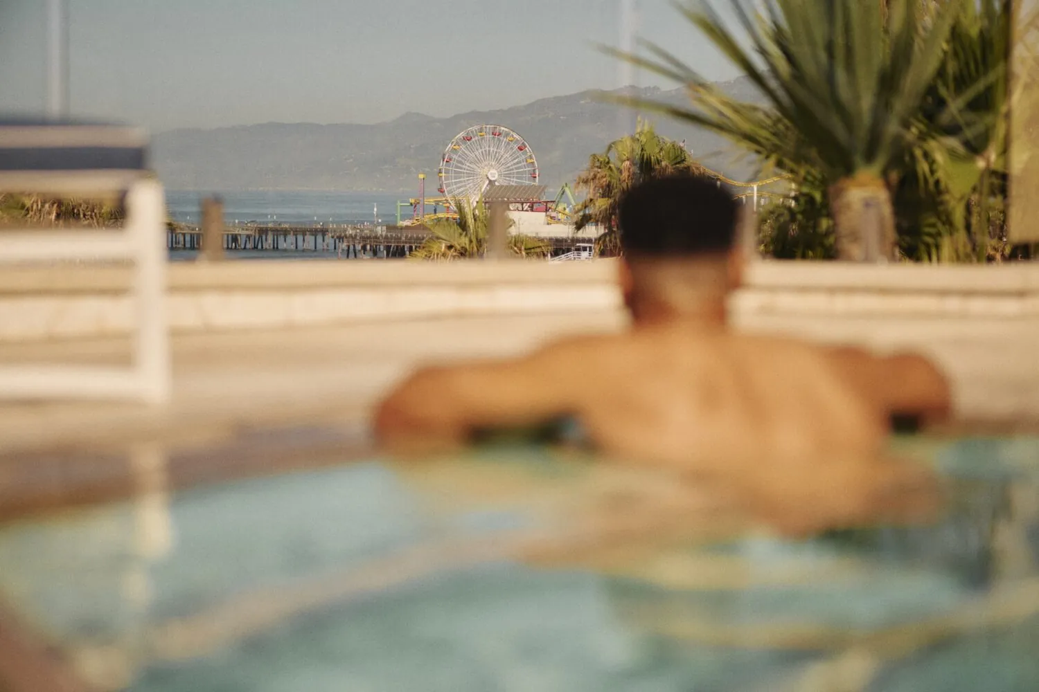 man in pool with a sharp focus on the Santa Monica Pier and Farris wheel
