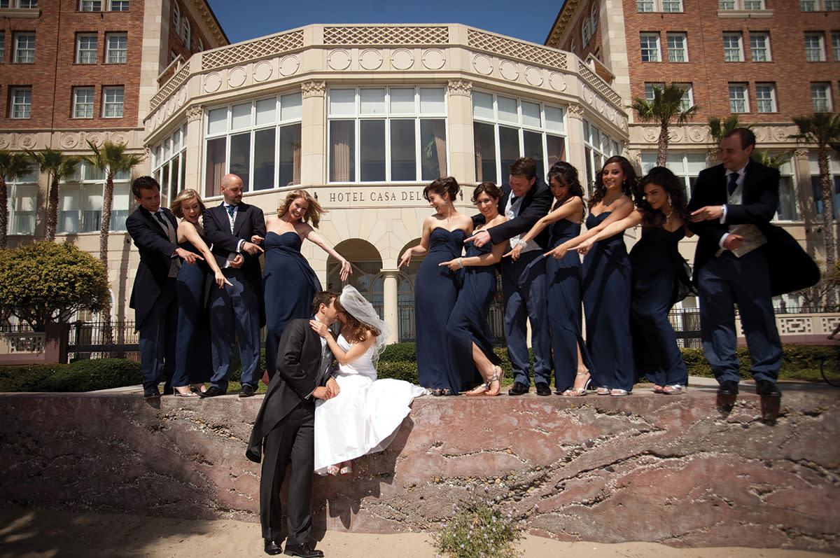 wedding party in front of the hotel with the couple kissing