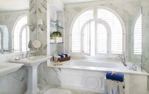 Pacific View suite's bathroom with white marble, freestanding tub, arched windows, and vanity sink.