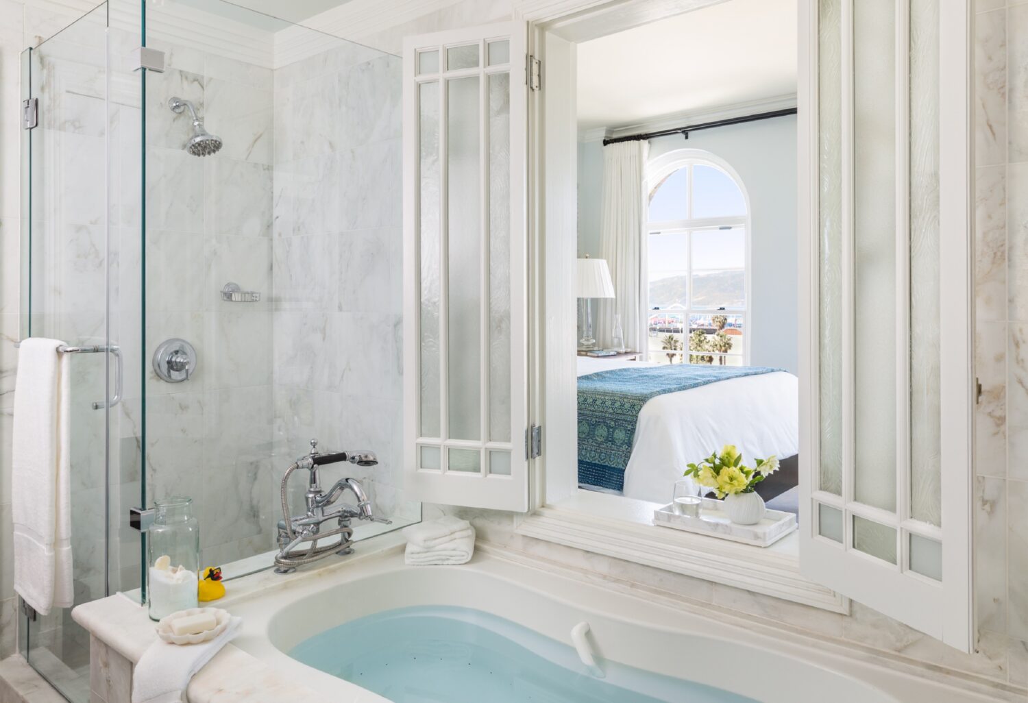 marble bathroom with window peering into the room with bed