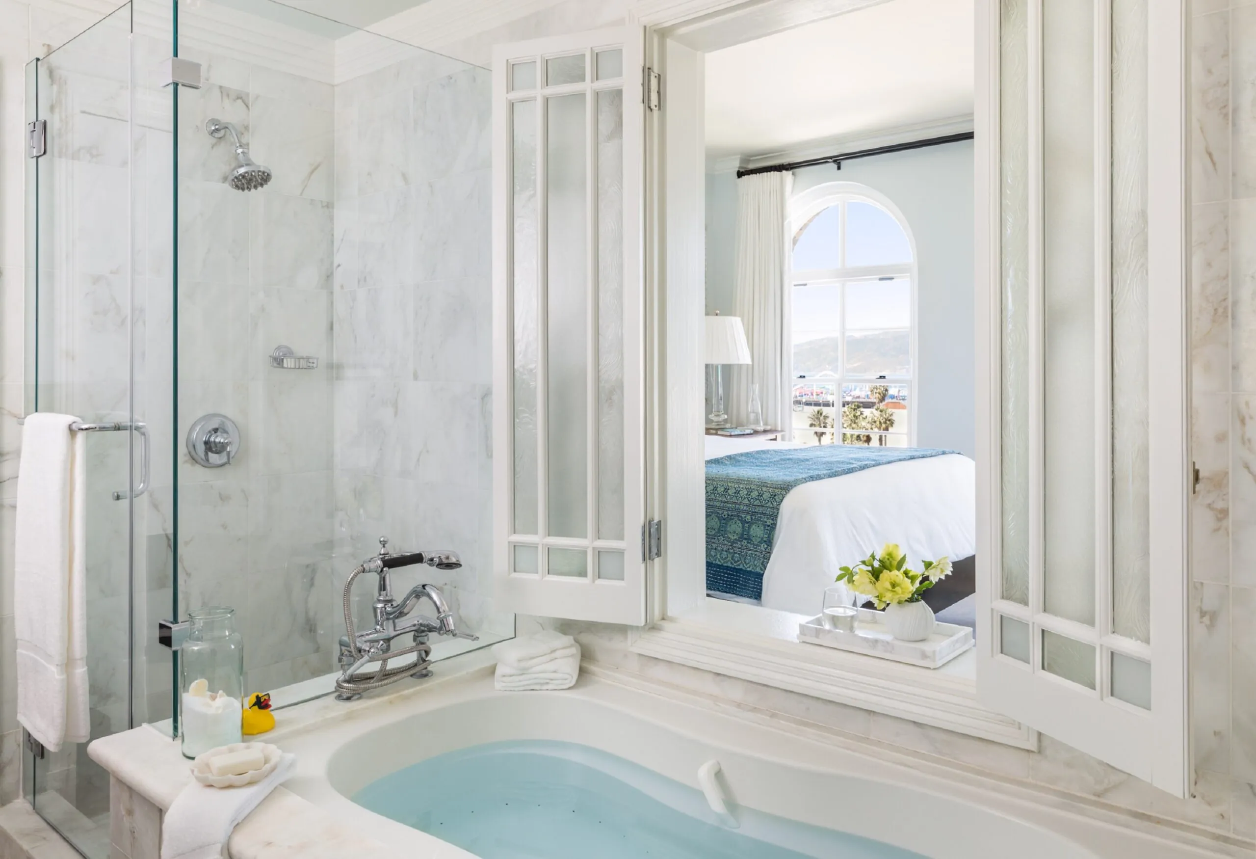 marble bathroom with window peering into the room with bed