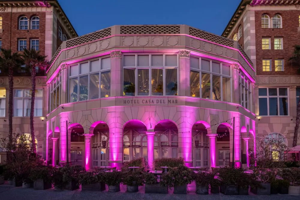 External view of a Hotel Casa del Mar event venue illuminated with pink lights at dusk.