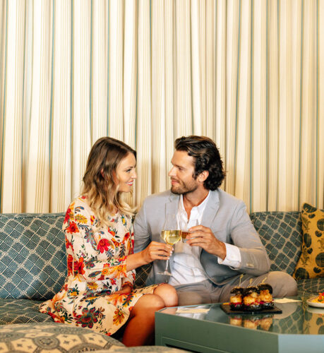 A man and woman toast with wine and whiskey glasses, gazing at each other in the Lobby Lounge.