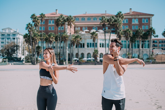A woman and man on the beach stretching for a yoga class