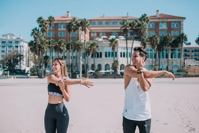 A woman and man on the beach stretching for a yoga class