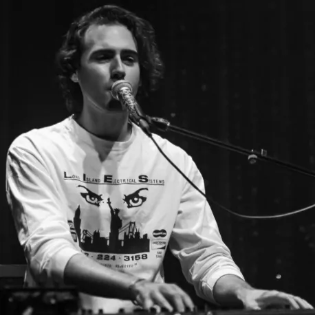 A man singing into a microphone on stage, wearing a long-sleeve shirt with a graphic design.