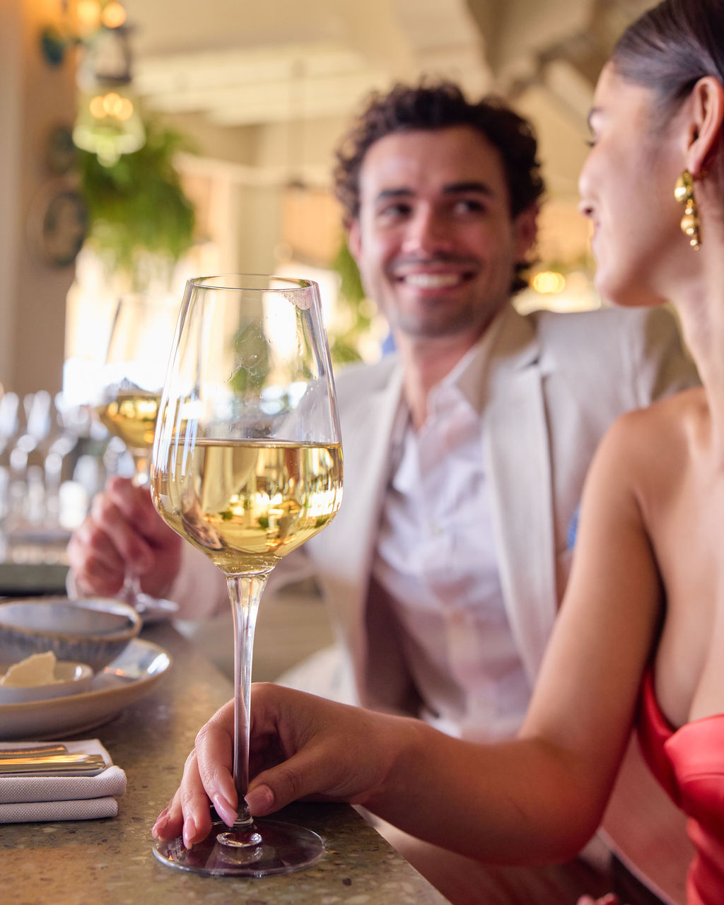 A couple smiling at a restaurant in Santa Monica, holding a glass of white wine at their table.