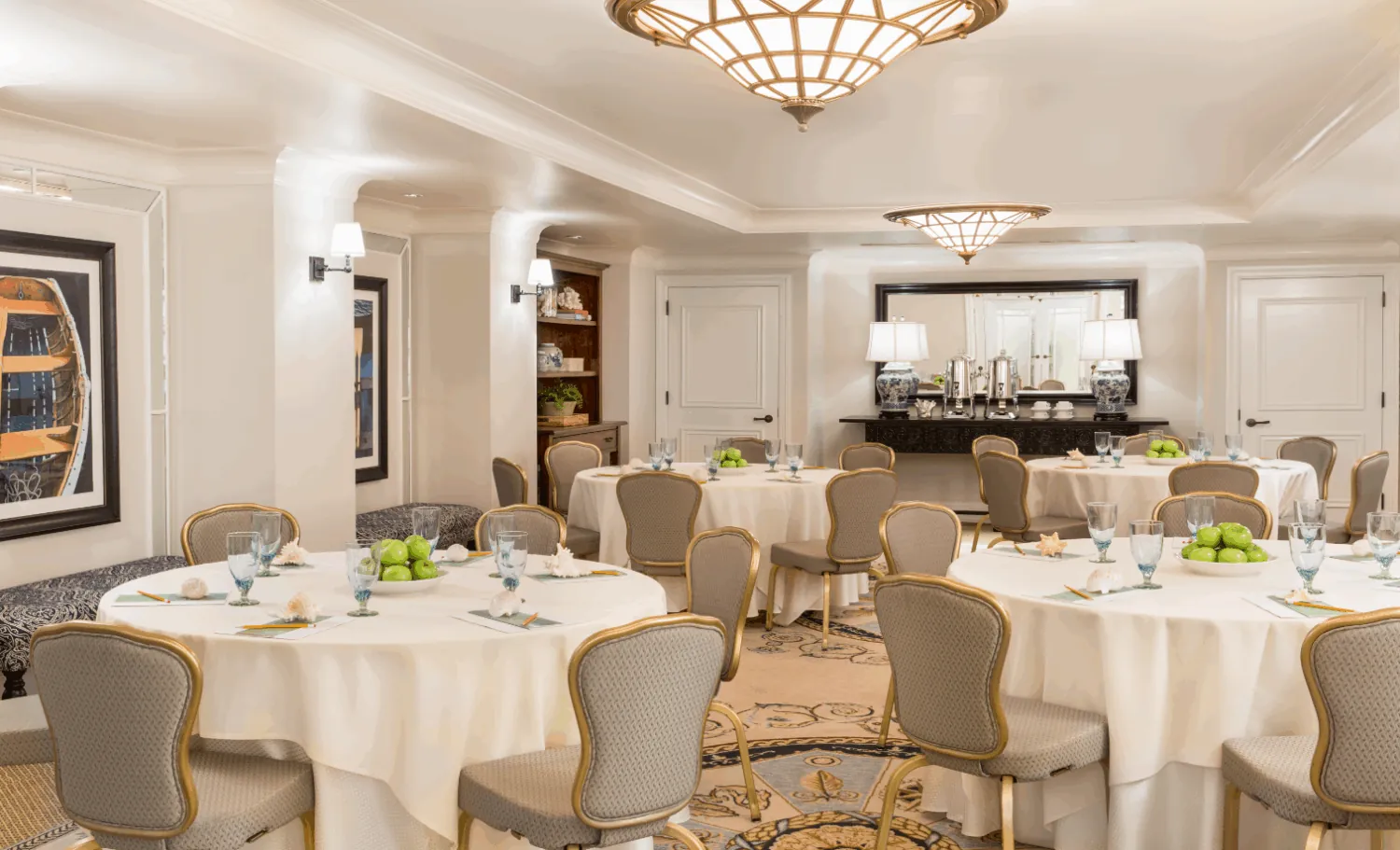 Elegant banquet hall with round tables set with green apples, glassware, and gray chairs.