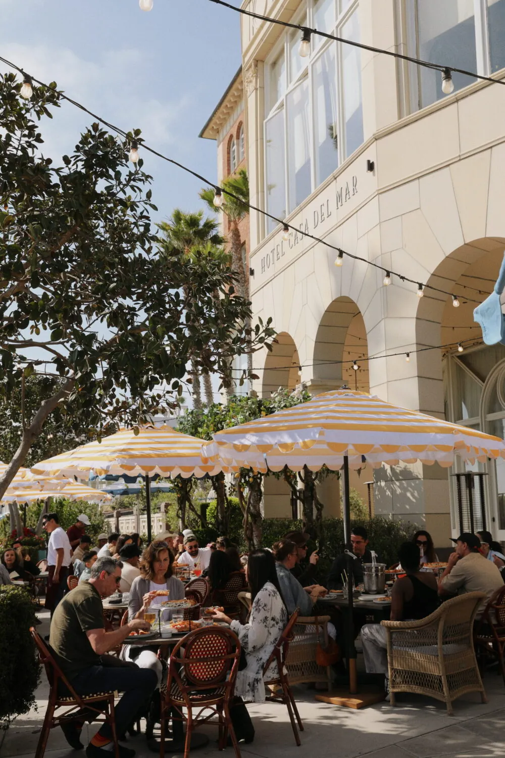 Outdoor restaurant at Hotel Casa del Mar with striped umbrellas, people dining under string lights.