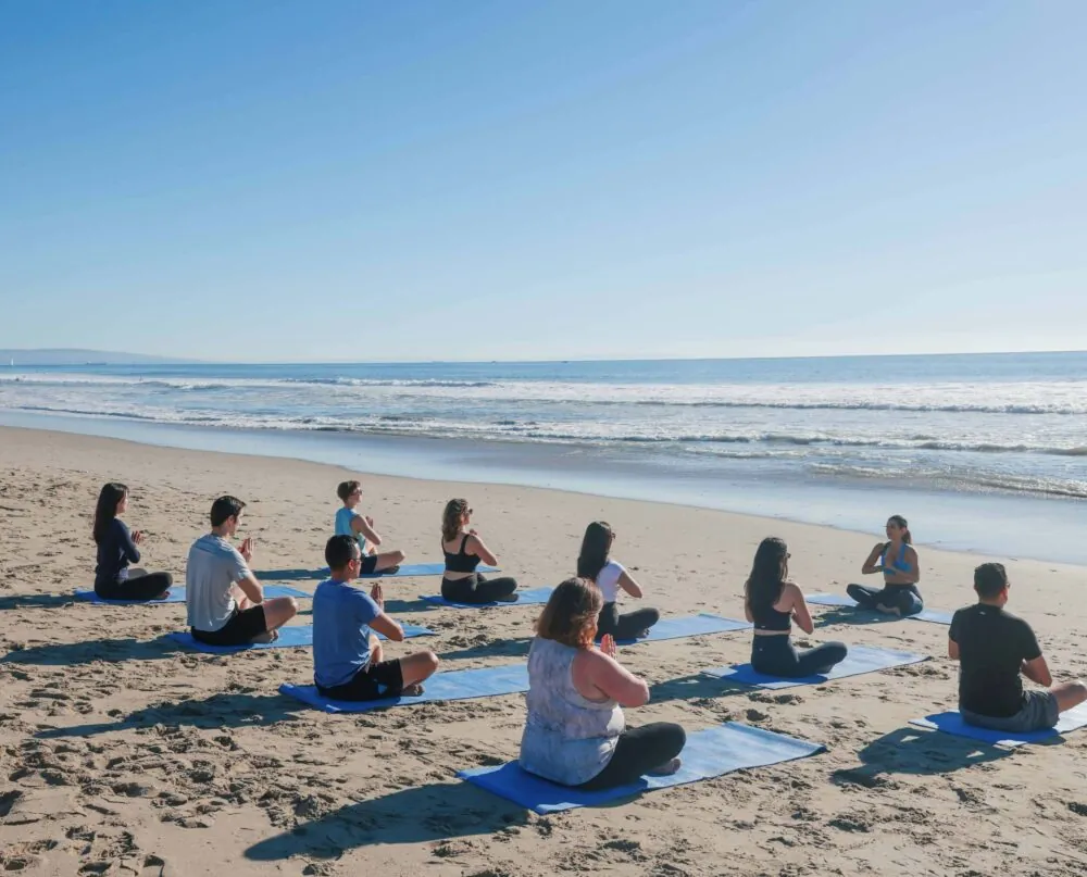 A group practicing yoga on blue mats at Santa Monica beach.