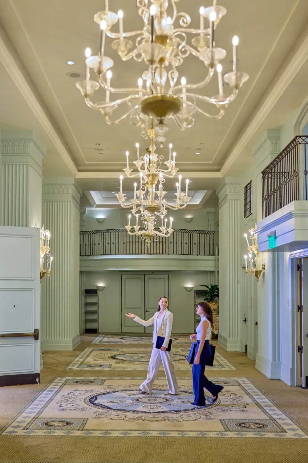 Two women walking in Hotel Casa del Mar grand hallway with ornate chandeliers.