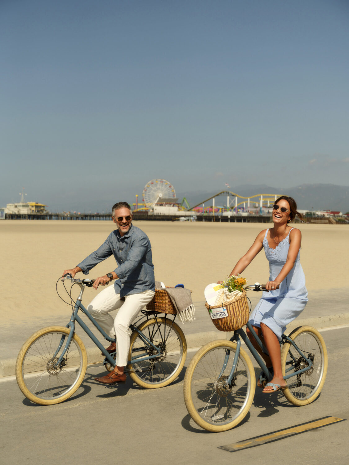 A couple enjoying a bike ride on the beach, with the Santa Monica Pier in the background.