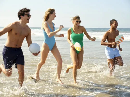 Group of friends playing in the surf, having fun with a ball and paddles at the beach.
