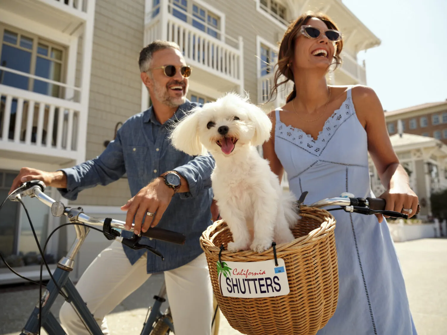 Man and woman riding bikes, dog in a basket, smiling and enjoying the day.