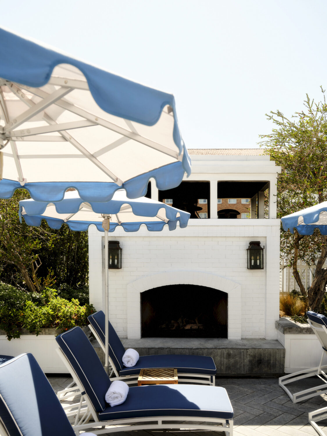 A row of lounge chairs under blue umbrellas, with a white brick fireplace in the background.