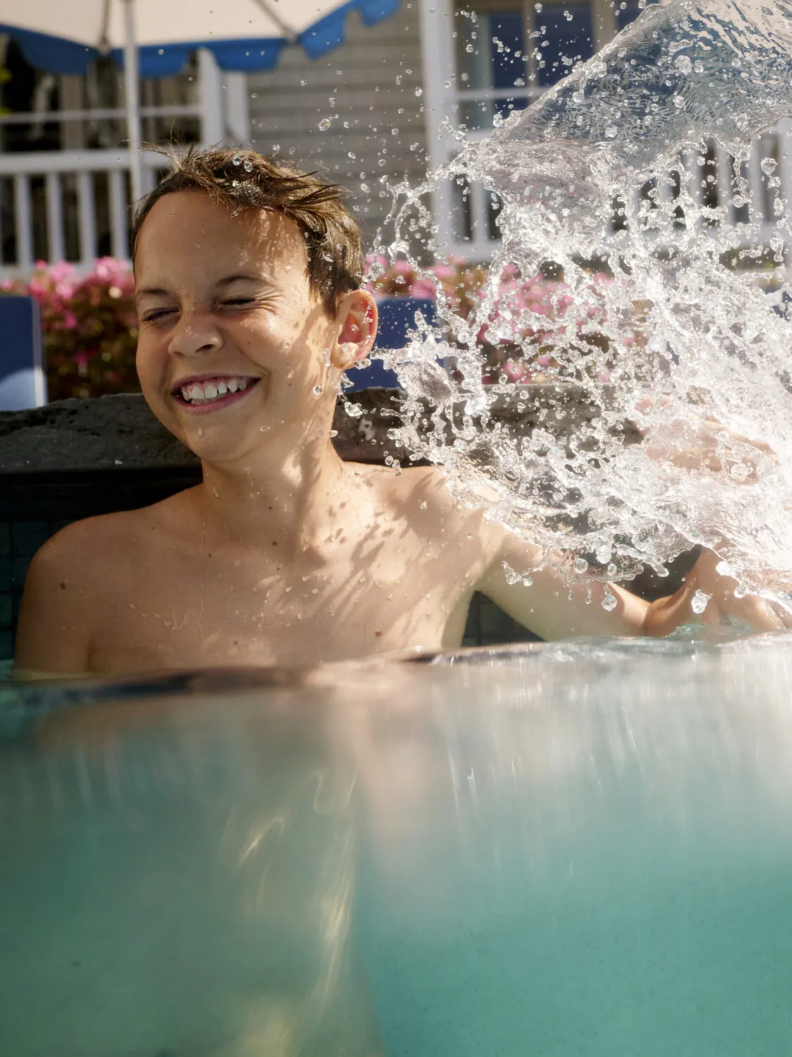 A boy smiles while water splashes around him in a pool, enjoying the moment.