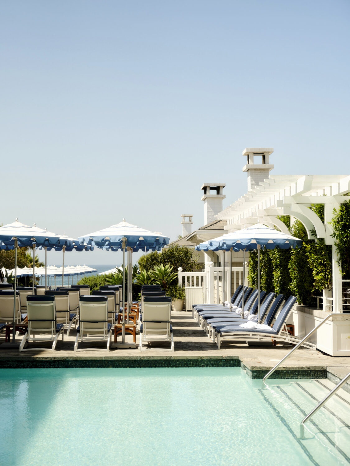 Poolside lounge chairs with blue umbrellas and a white building in the background.
