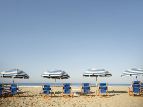 Empty beach chairs with striped umbrellas on a sunny beach, overlooking the ocean.