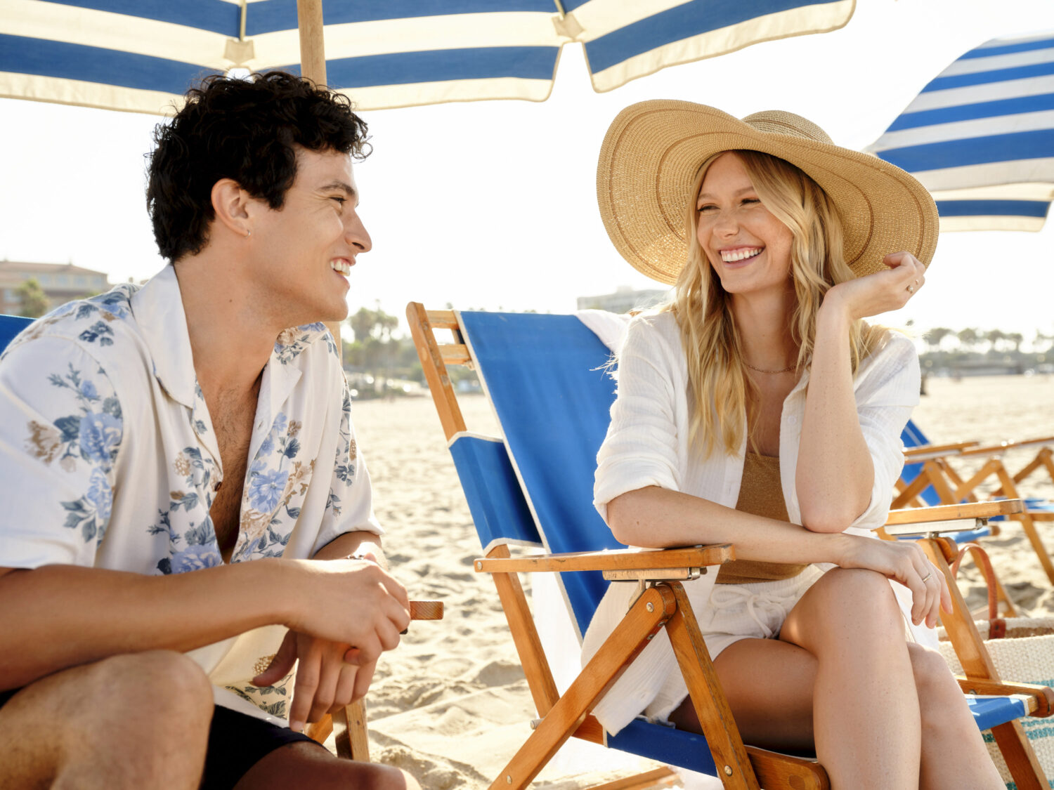 A joyful couple laughing together at the beach under an umbrella.