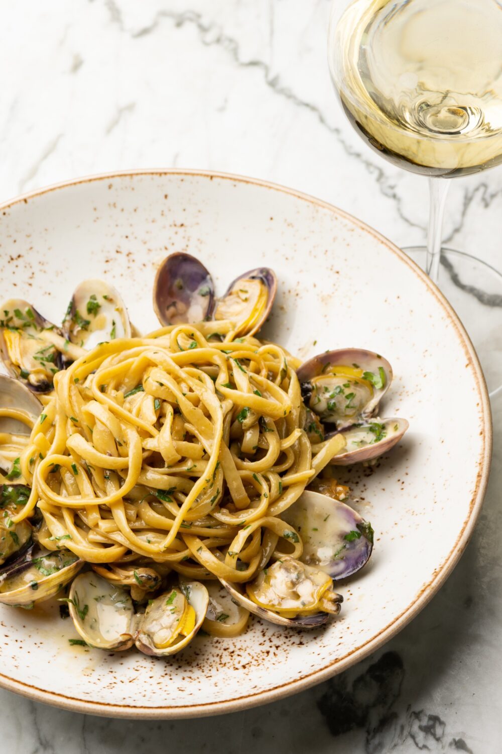 Plate of linguine pasta with clams in sauce, garnished with parsley, and a glass of white wine.