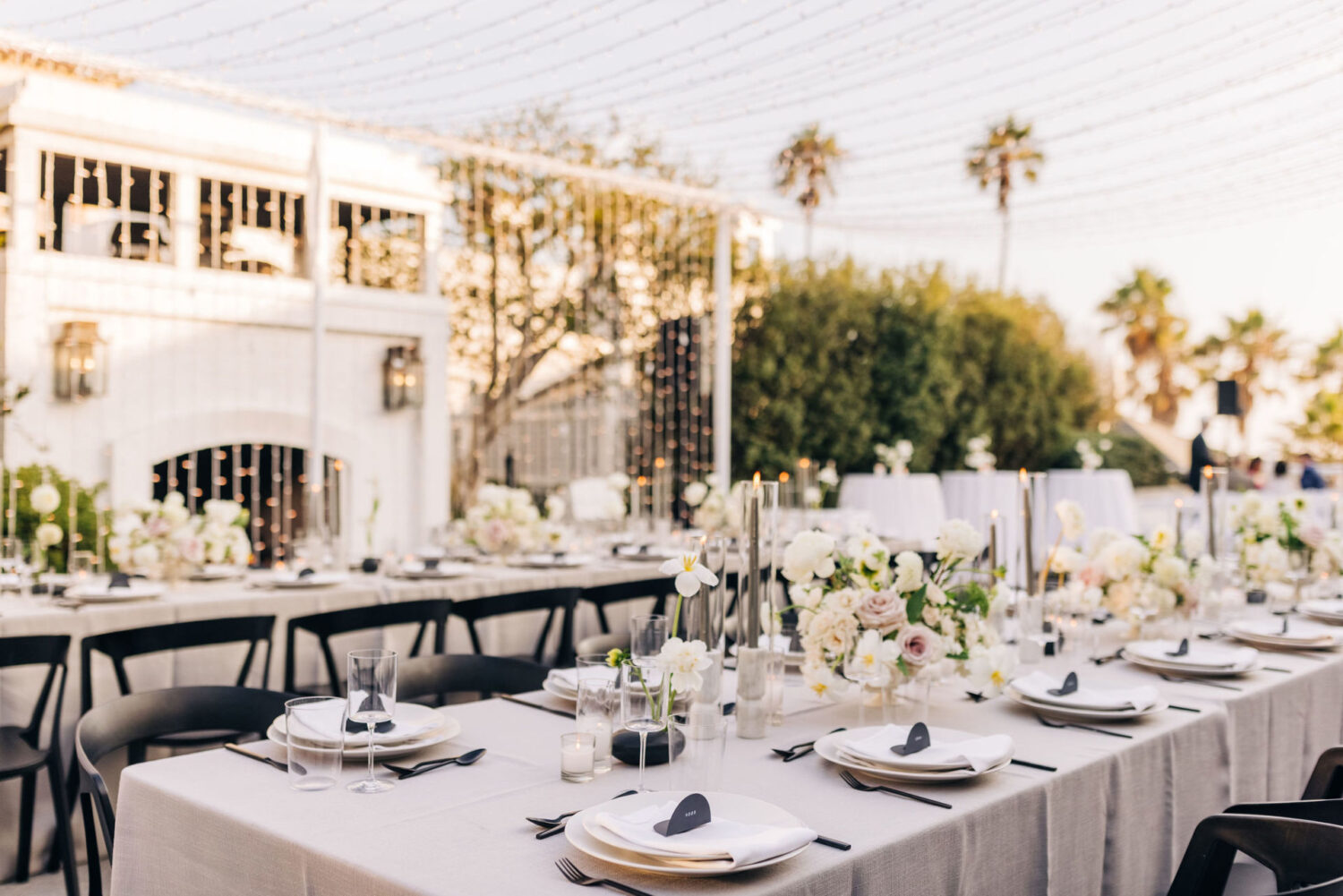 Elegant outdoor dining setup with floral arrangements, candles, and twinkling string lights.