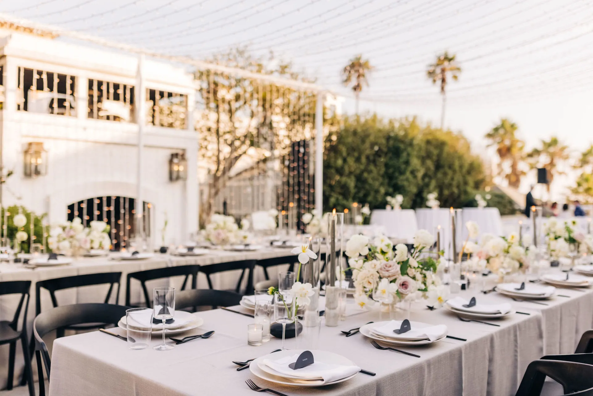 Elegant outdoor dining setup with floral arrangements, candles, and twinkling string lights.