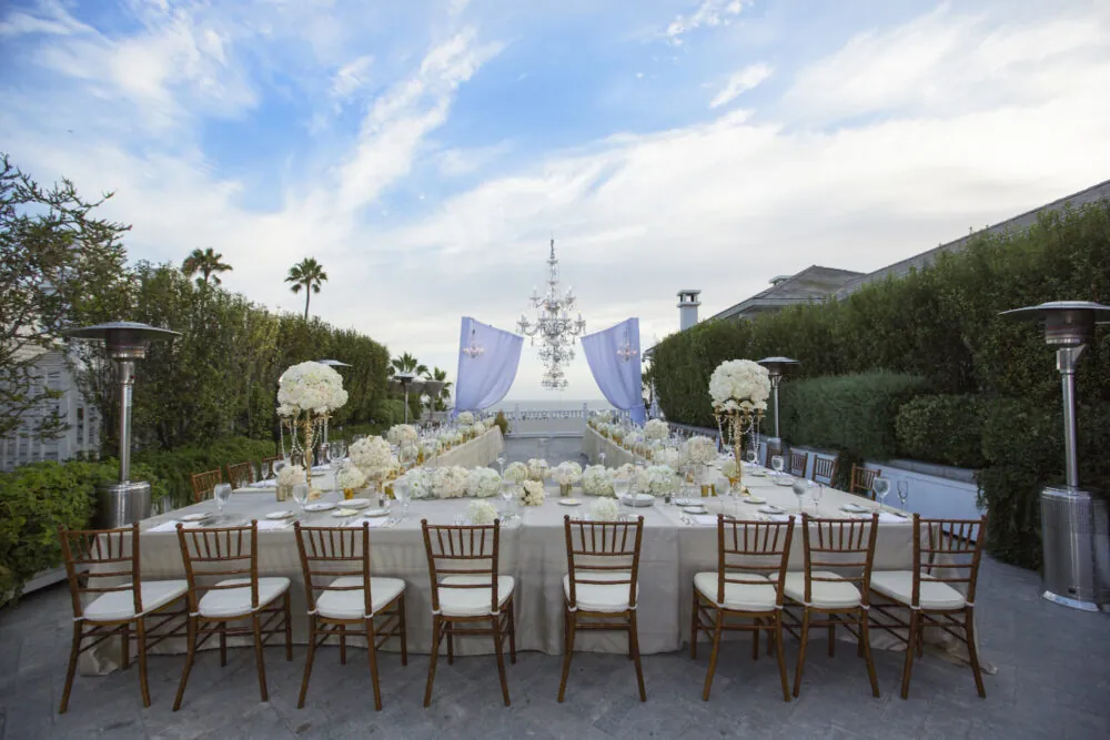 Stunning outdoor wedding reception with chandeliers, floral centerpieces, and a coastal backdrop.
