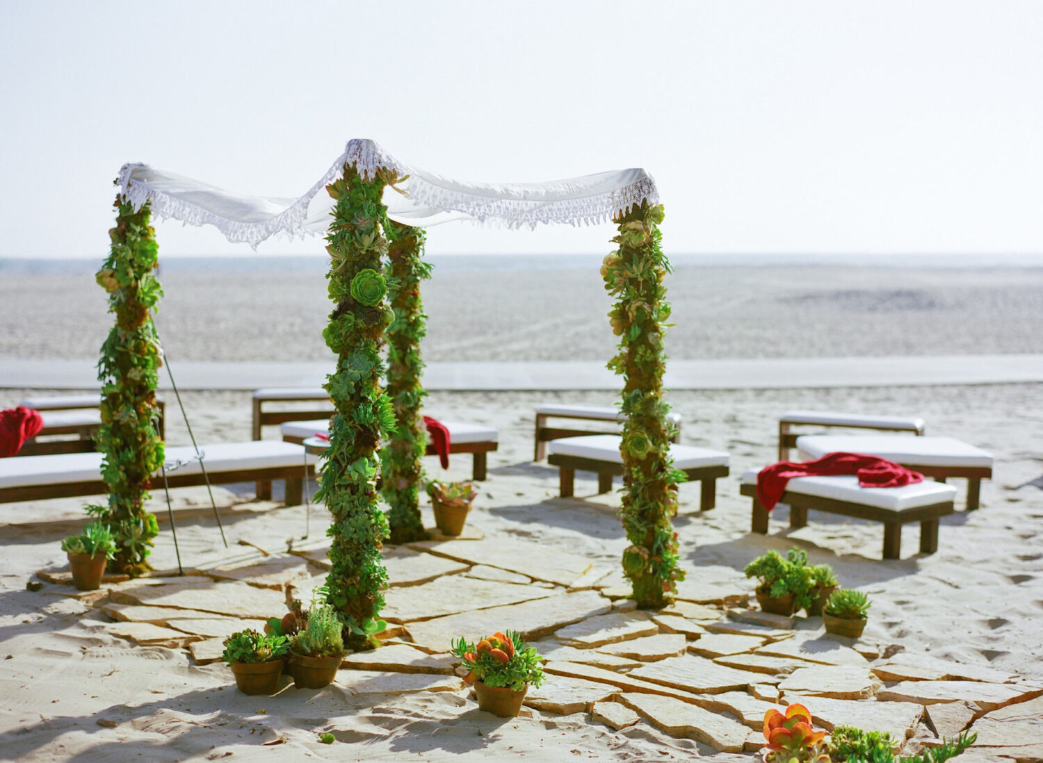 Beachside wedding with a succulent canopy, stone floor, and lounge seating.