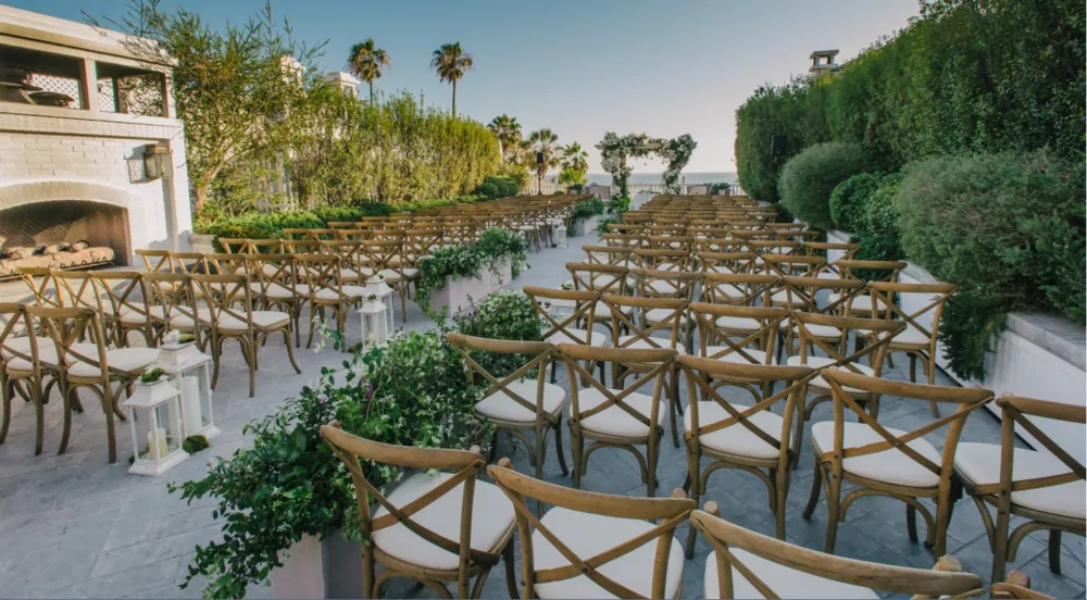 Elegant outdoor wedding ceremony setup with wooden chairs, lush greenery, and ocean views.