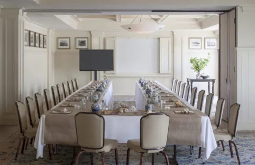 Conference room with long table, plants, projector and elegant decor in soft tones.